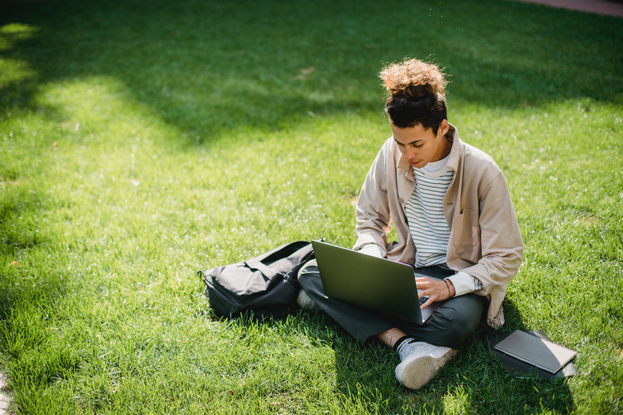 Student with book and laptop in grass